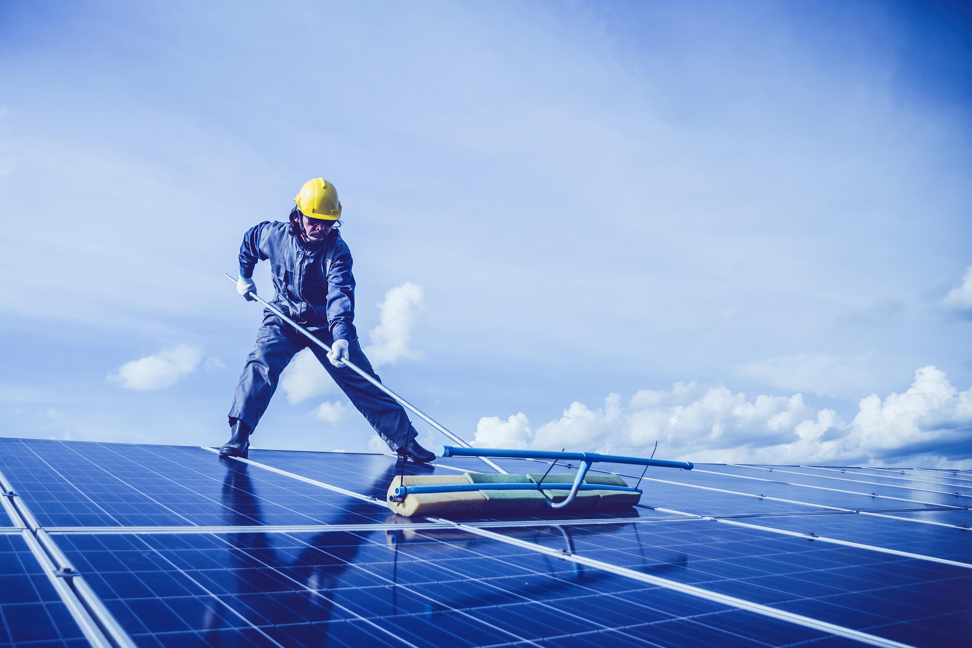 Técnico con arnés y escoba rotativa limpiando módulos fotovoltaicos en cubierta